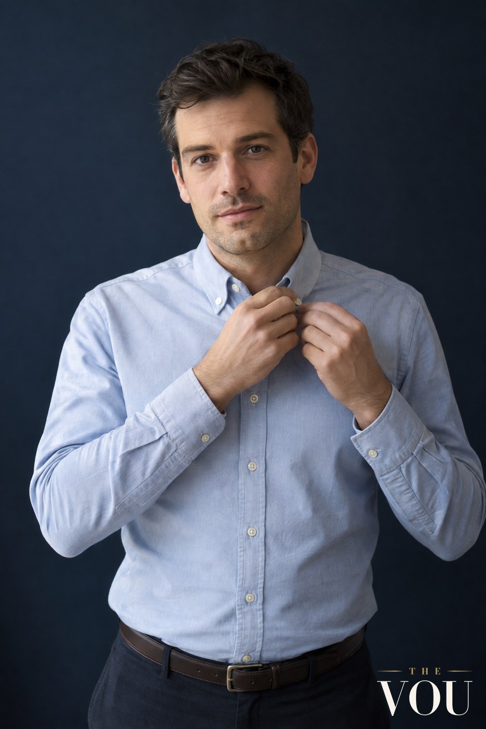 A man in a light blue Oxford cloth shirt with a button-down collar, its collar points buttoned to the shirt front, fastening the top button.