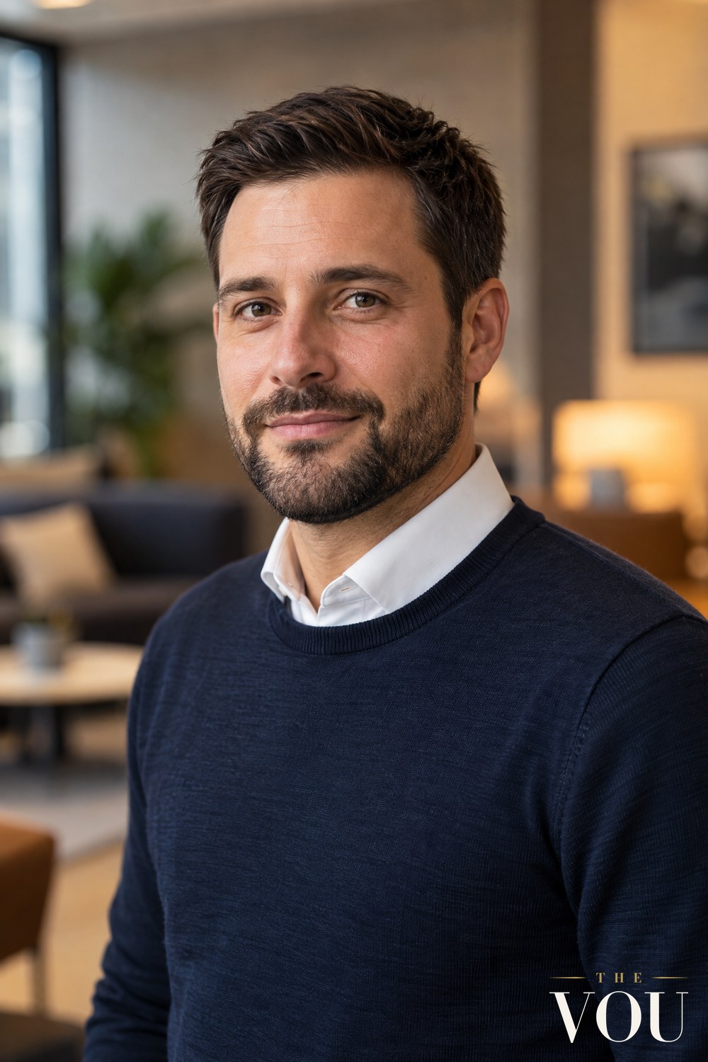 A man with a neat short boxed beard with crisp cheek lines and a clean neckline, wearing a navy knit over a white shirt collar.